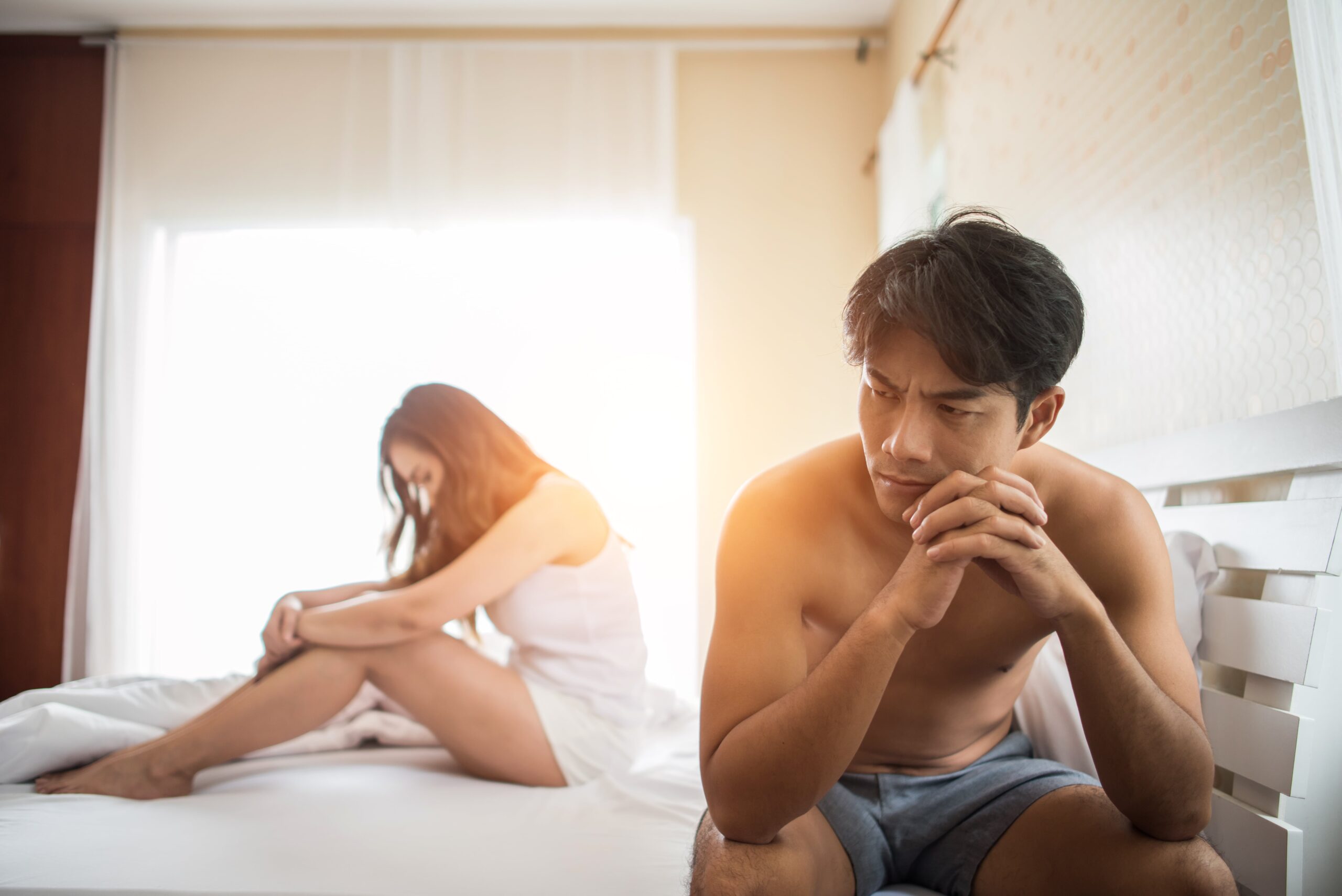 A distressed man sitting on the edge of a bed, illustrating the emotional strain PTSD can place on a romantic relationship